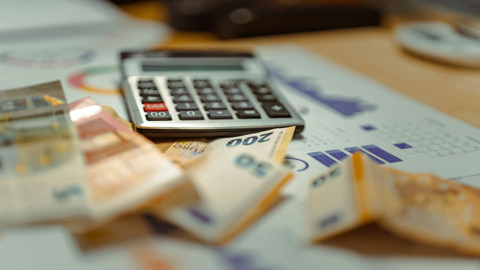 Dokumente zur finanziellen Analyse und Euroscheine neben einem Taschenrechner auf einem Tisch.